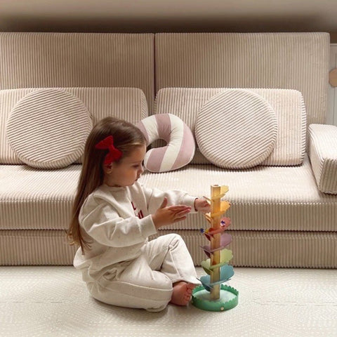 1. Young girl playing with Woopie Let's Go Green musical rainbow wooden ball track on a beige sofa