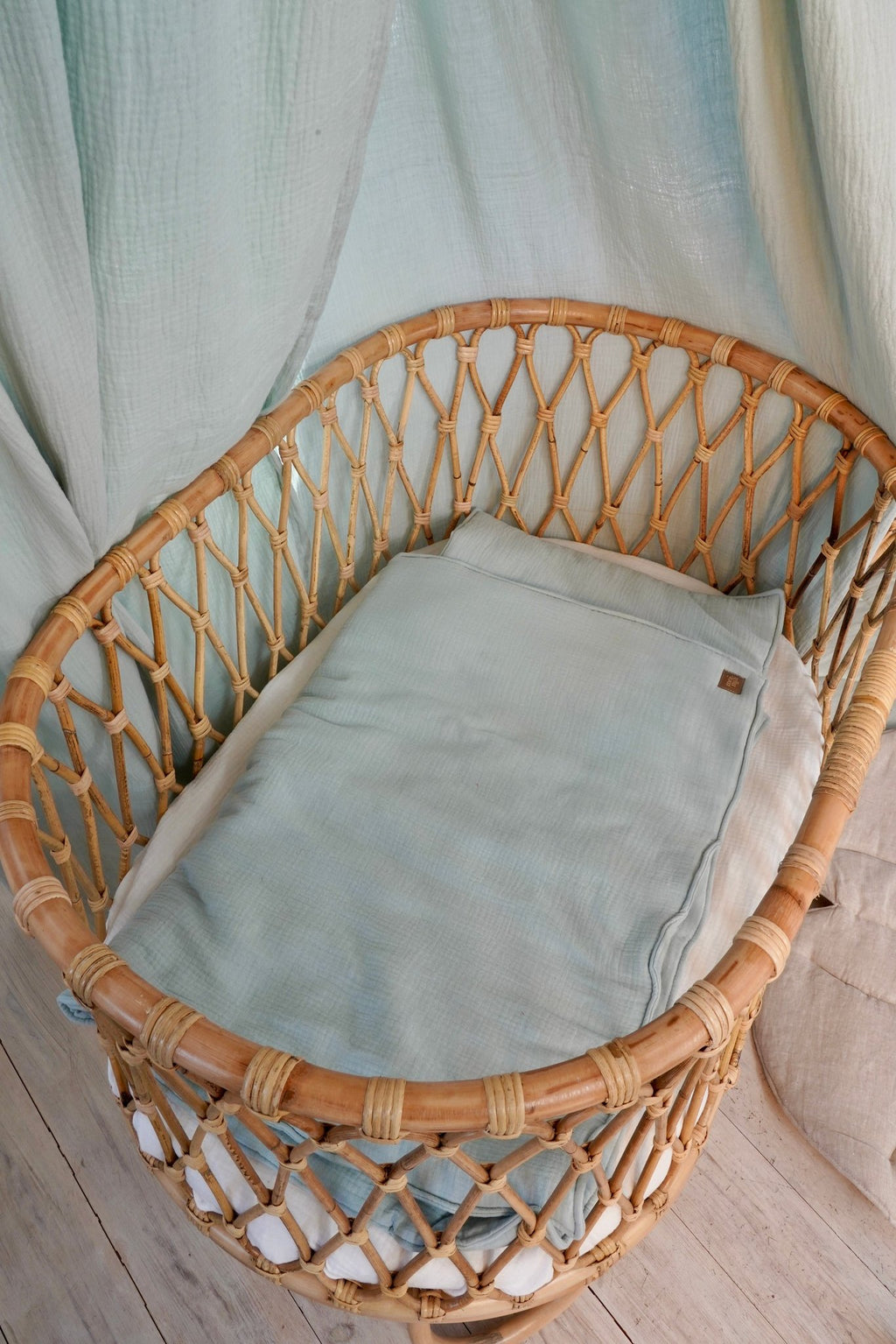 1. Mint muslin baby blanket and pillow set in a wicker crib with soft draped fabric background