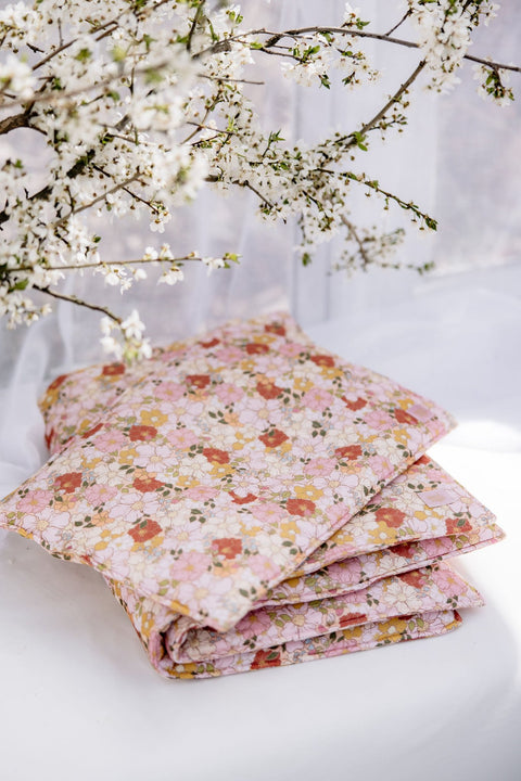 4. Stacked floral muslin baby blankets in pink, yellow, and white on a white surface with blooming branches