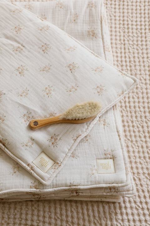3. Close-up of muslin baby blanket and pillow set with boho flower print, featuring Moi Mili logo and baby brush