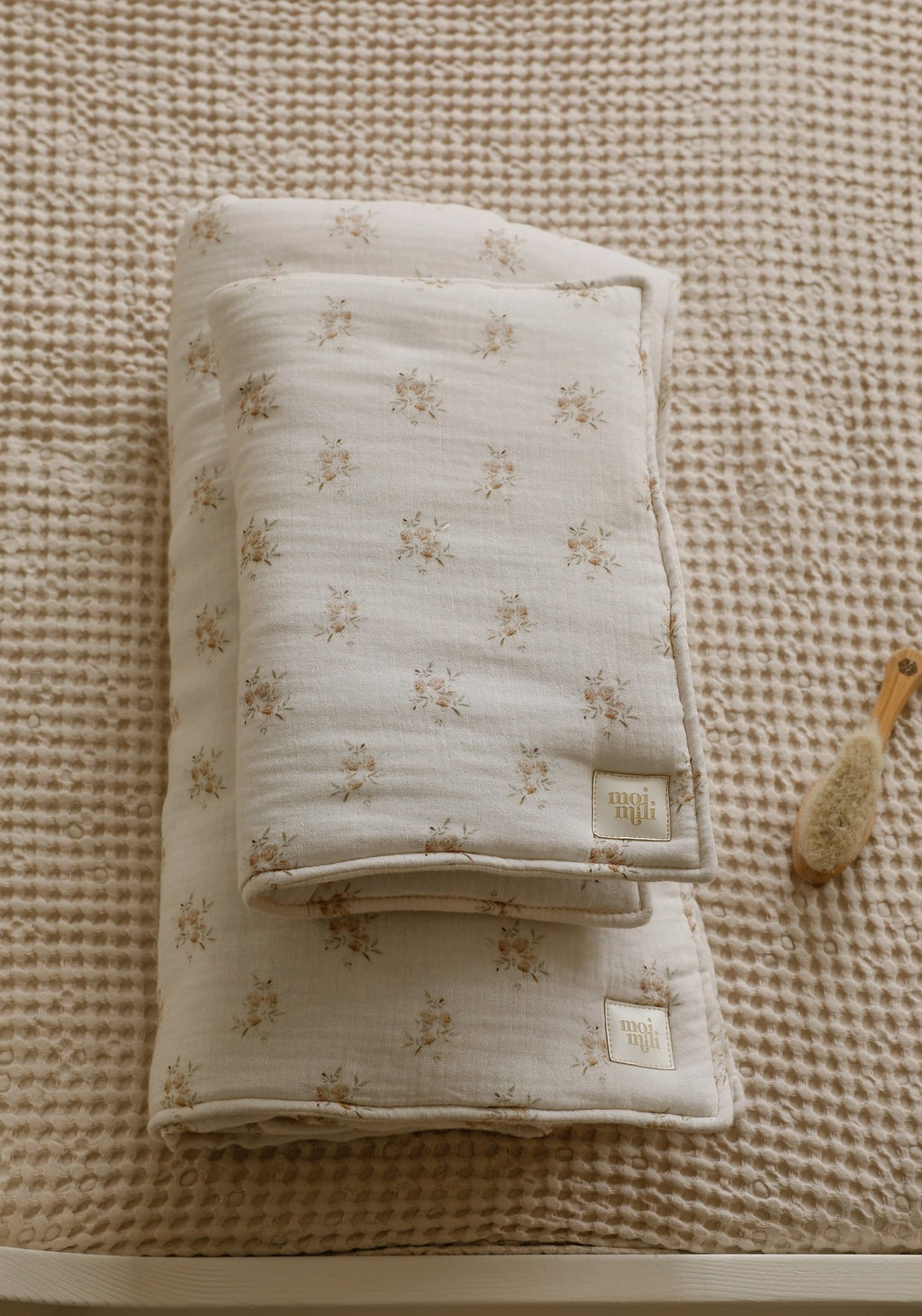 5. Flat lay of folded muslin baby blanket and pillow set with boho flower print on a textured beige surface