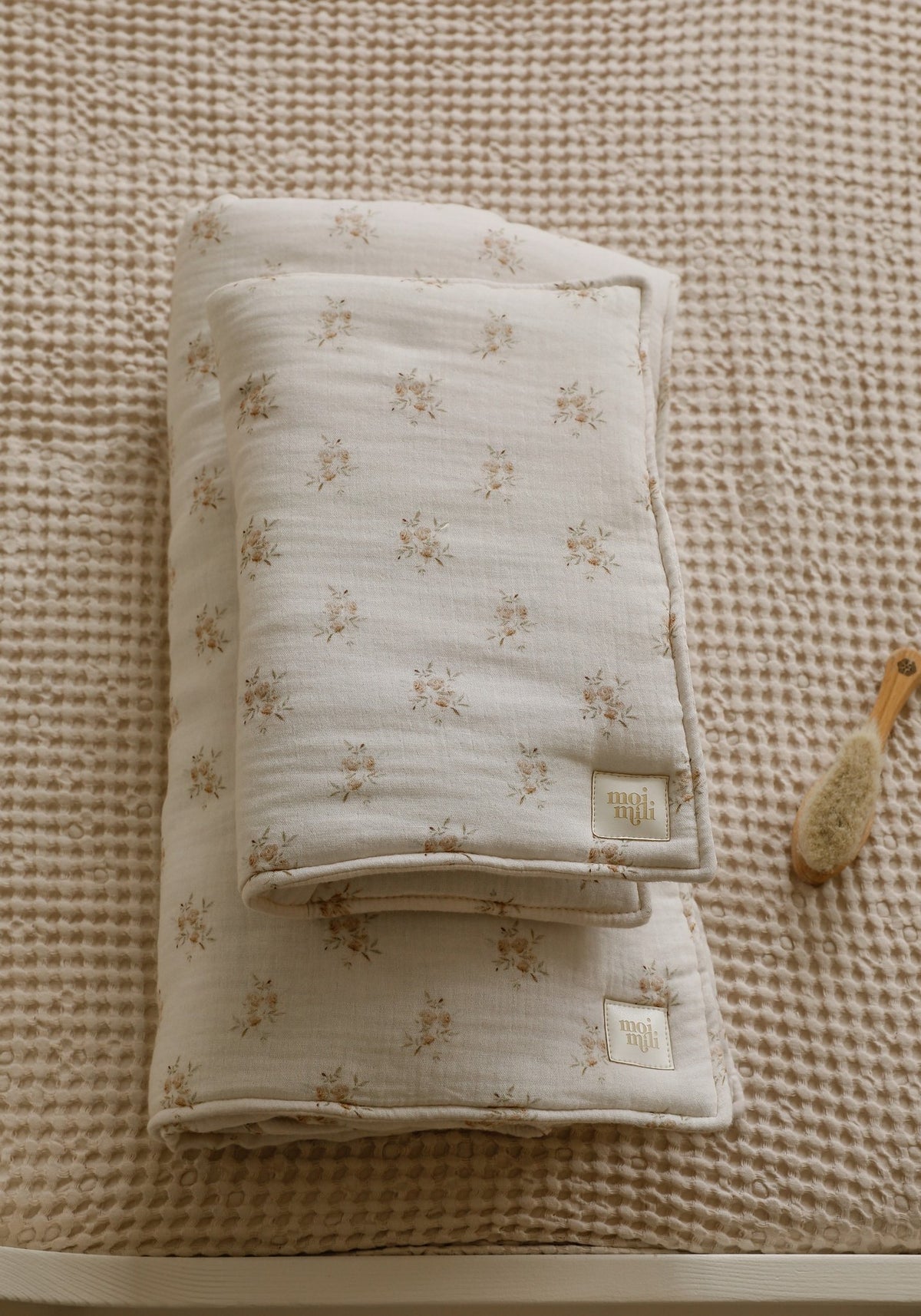 5. Flat lay of folded muslin baby blanket and pillow set with boho flower print on a textured beige surface