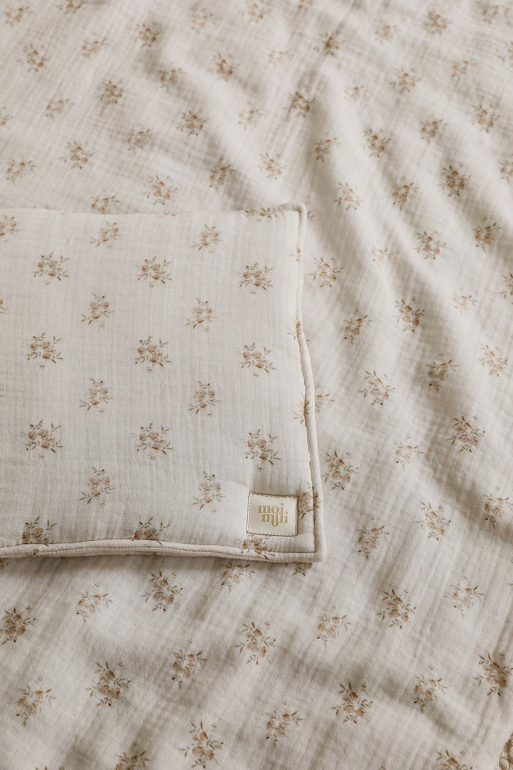 4. Detail shot of muslin baby blanket and pillow with boho flower print, showing fabric texture and Moi Mili logo