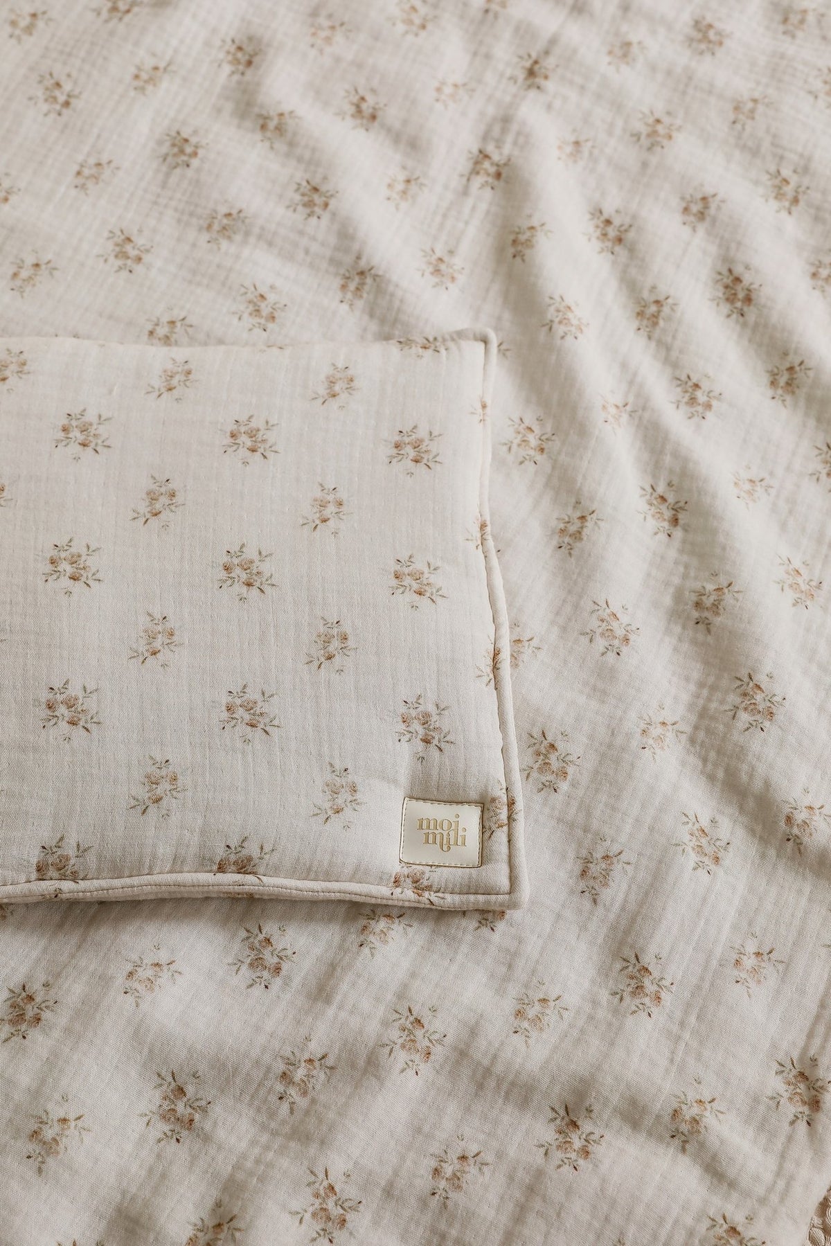 4. Detail shot of muslin baby blanket and pillow with boho flower print, showing fabric texture and Moi Mili logo