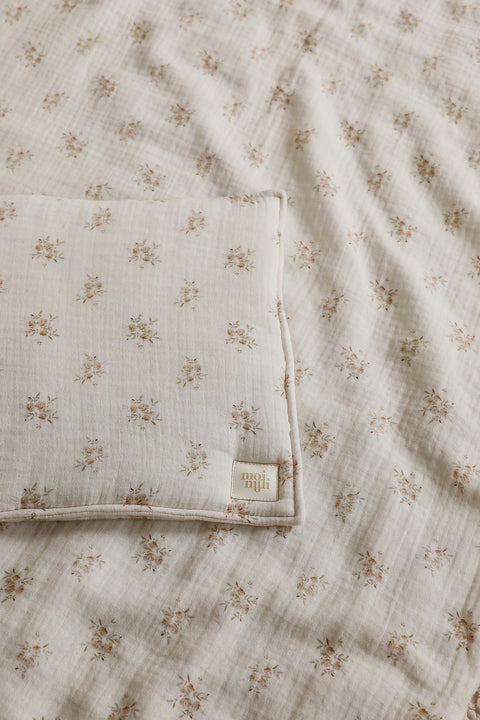 4. Detail shot of muslin baby blanket and pillow with boho flower print, showing fabric texture and Moi Mili logo