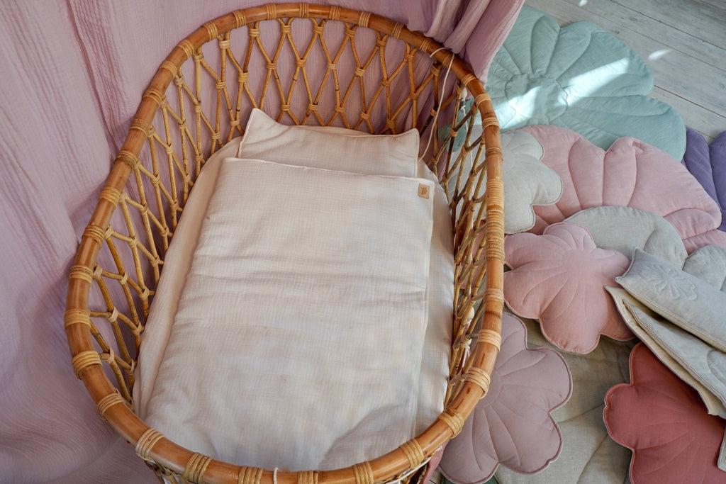 3. Cream muslin baby blanket and pillow set in a wicker crib with pastel cushions