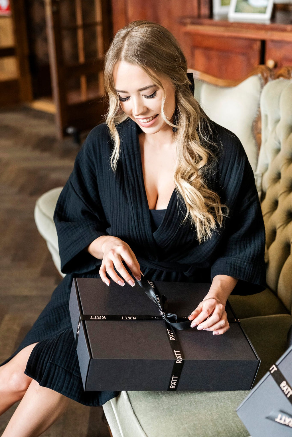 5. Women's black muslin kimono by RÄTT, worn by a model sitting on a sofa with a gift box