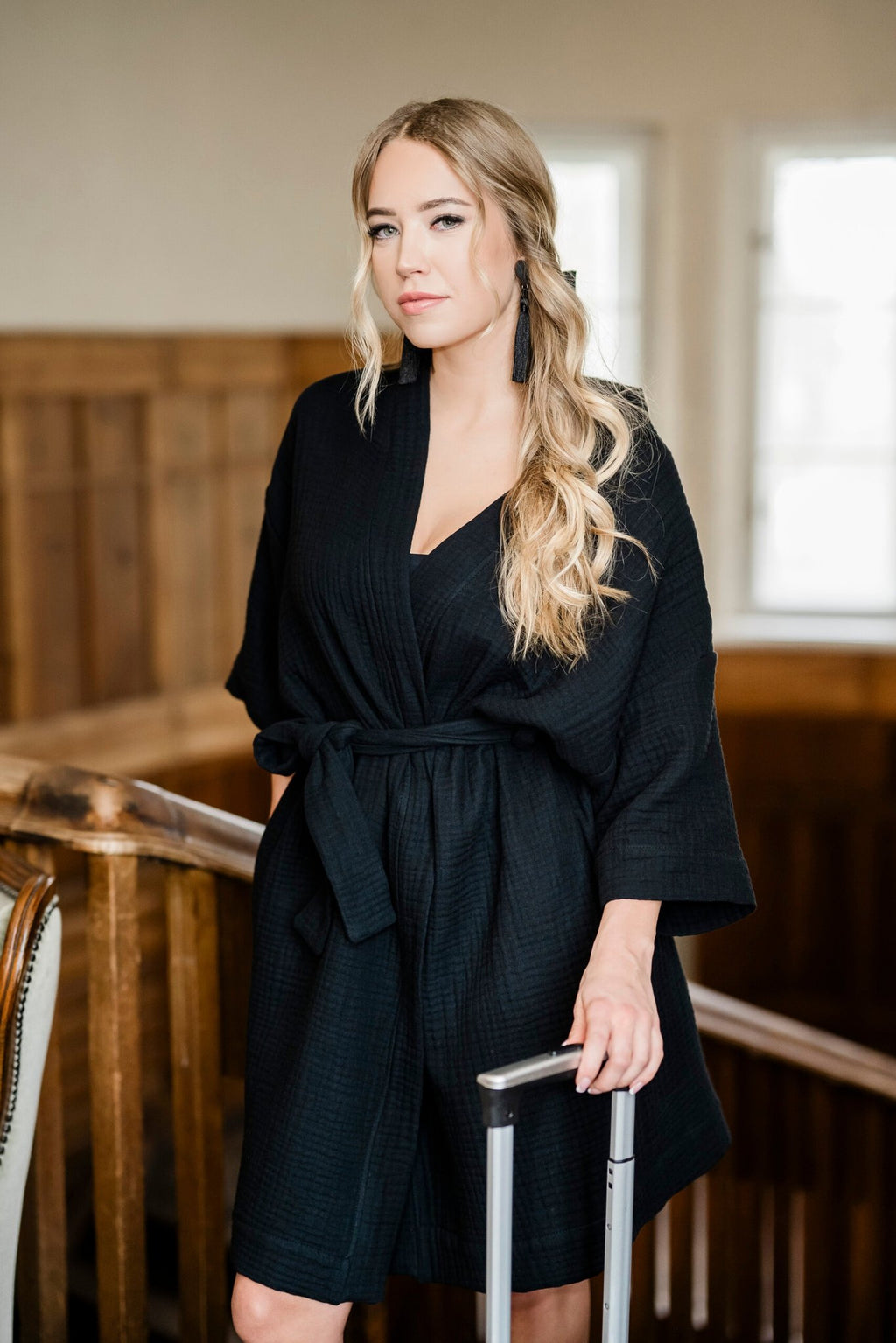 7. Women's black muslin kimono by RÄTT, worn by a model standing with a suitcase in a wooden interior