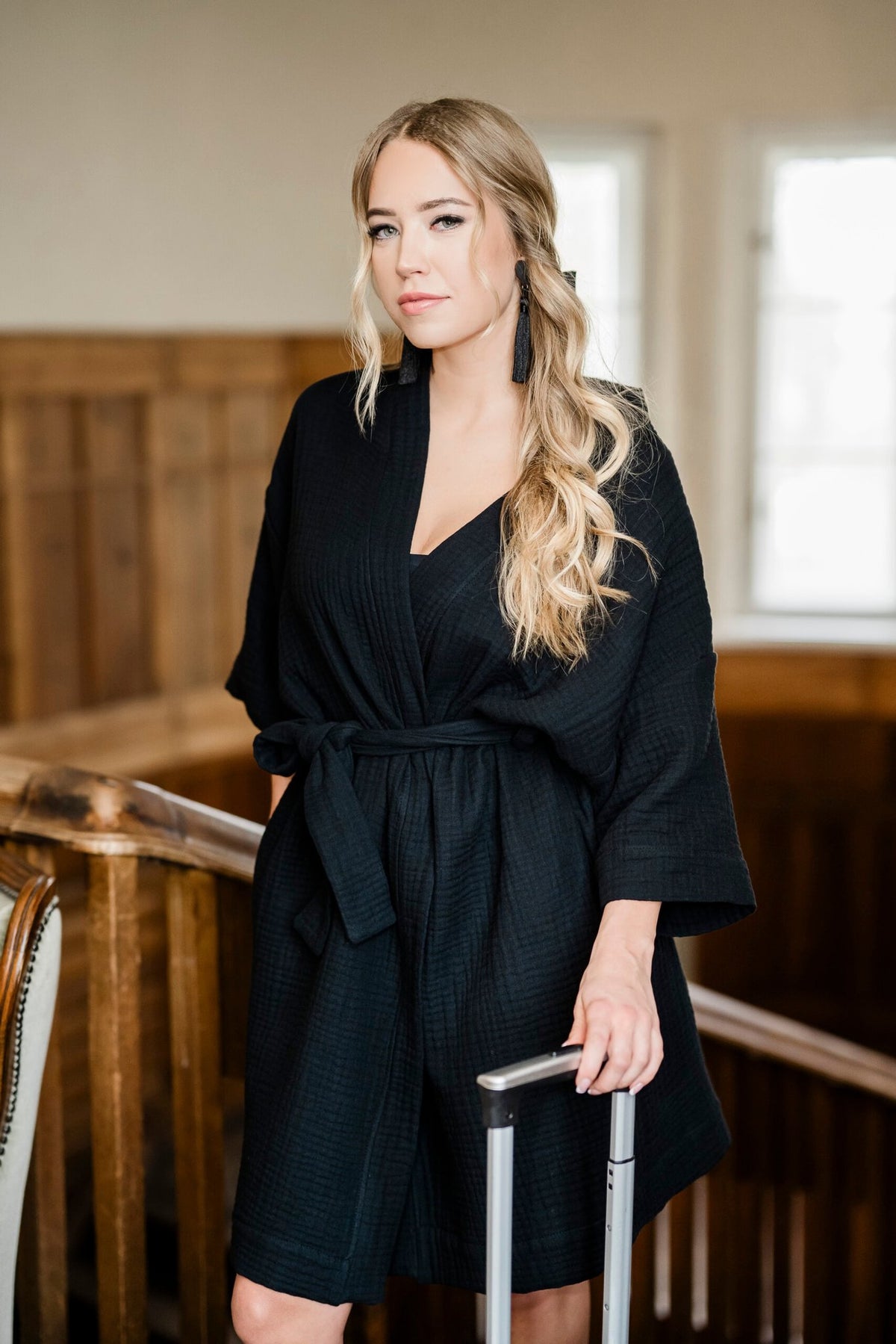 7. Women's black muslin kimono by RÄTT, worn by a model standing with a suitcase in a wooden interior