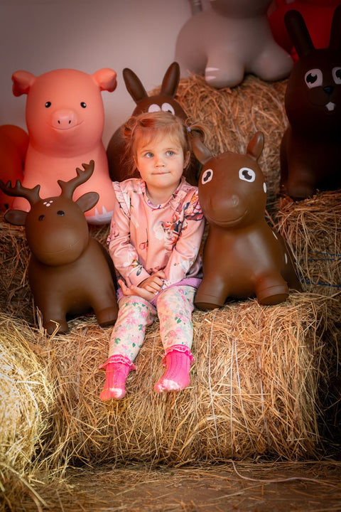 4. Girl sitting on hay with brown horse hopper toy and other animal toys in barn setting
