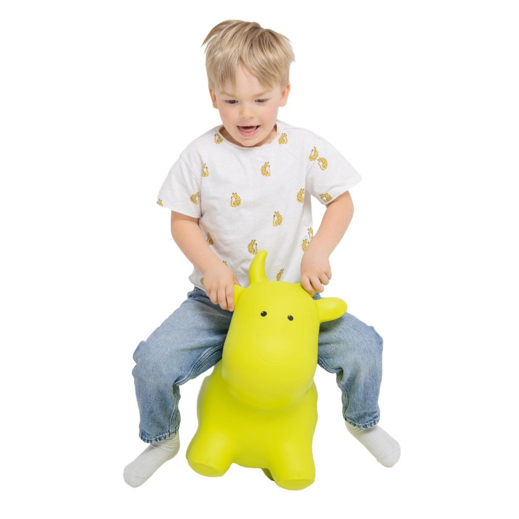 1. Child playing on green cow-shaped hopper toy wearing white shirt and jeans indoors