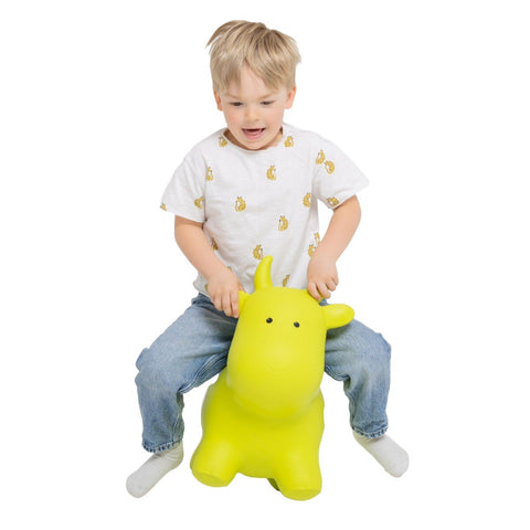 1. Child playing on green cow-shaped hopper toy wearing white shirt and jeans indoors