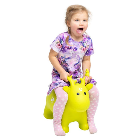 1. Young girl in a floral dress and pink polka dot tights riding a green moose-shaped hopper toy indoors, smiling and having fun