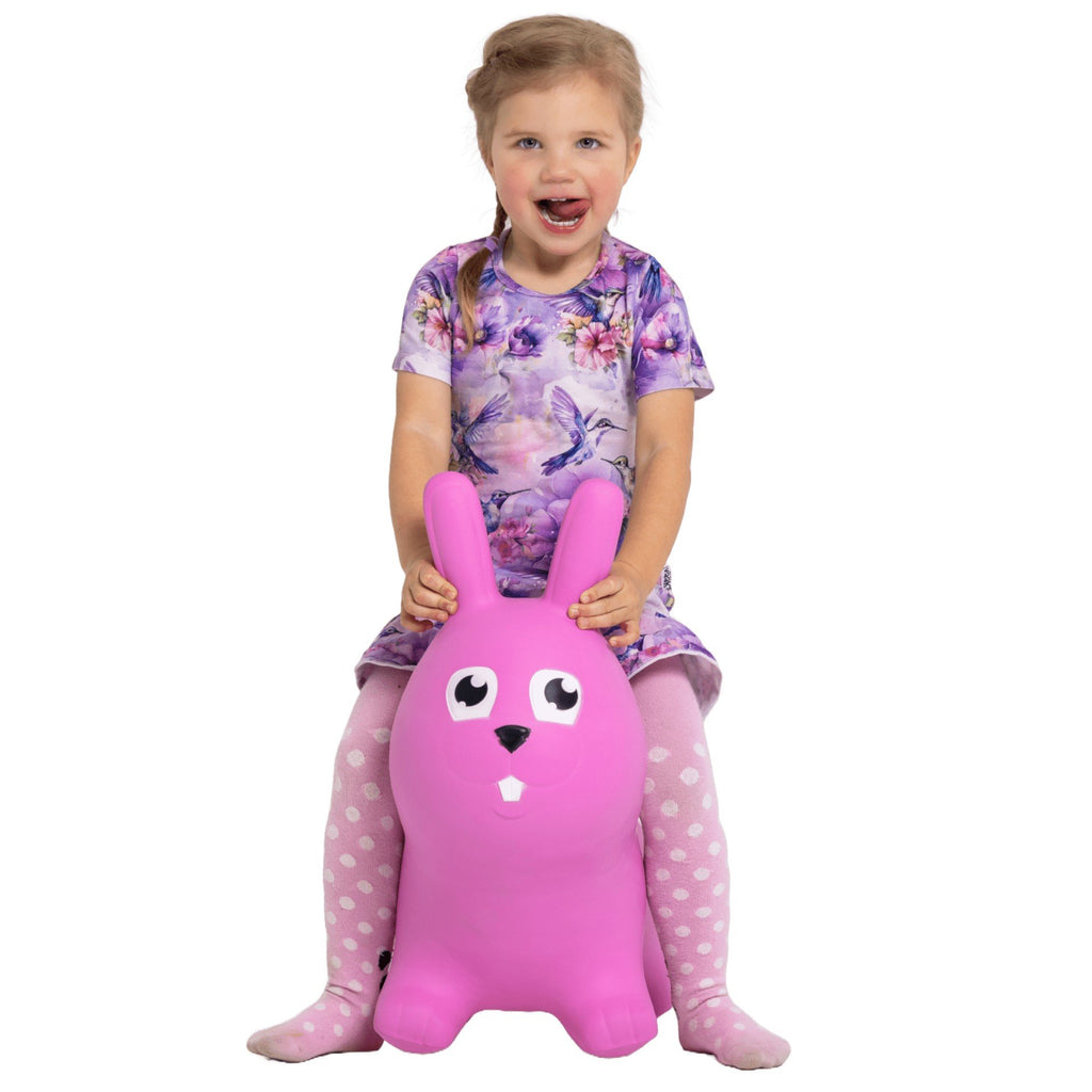 1. Young girl in floral dress and polka dot tights sitting on pink bunny hopper toy, smiling in studio setting