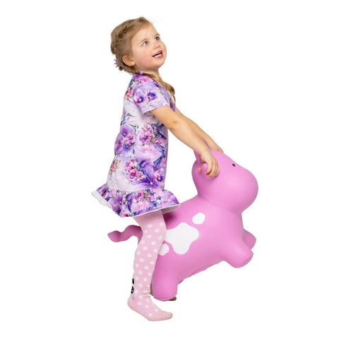 1. Young girl in floral dress and polka dot tights playing on pink cow-shaped hopper toy indoors