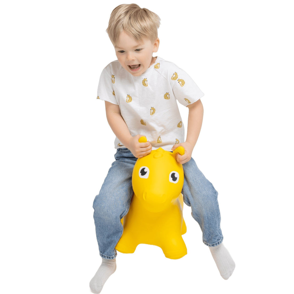 1. Child wearing white shirt and jeans joyfully bouncing on yellow horse-shaped hopper toy indoors