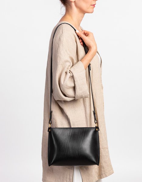 1. Woman holding black leather Stella Soomlais handbag with adjustable strap, beige outfit, studio setting