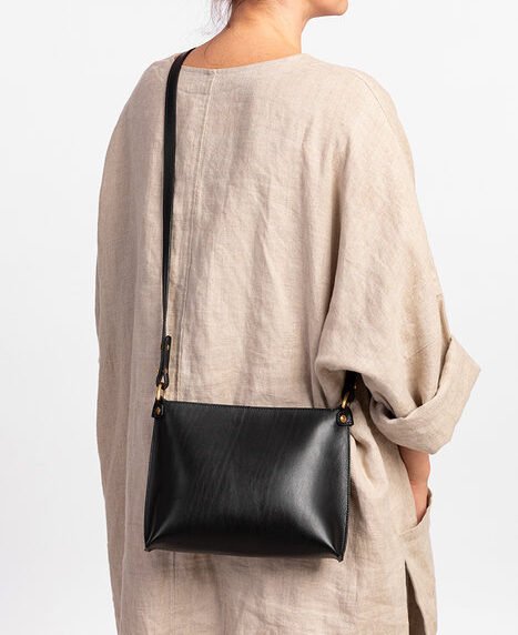 1. Woman wearing black leather Stella Soomlais handbag with adjustable strap over shoulder, beige outfit, studio setting