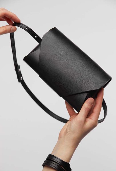 5. Hands holding black leather Stella Soomlais Capital of Plenty clutch-wallet with strap
