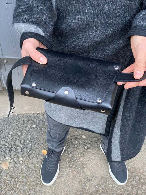 2. Person holding black leather Stella Soomlais shoulder bag with metal rivet details, wearing grey coat and sneakers