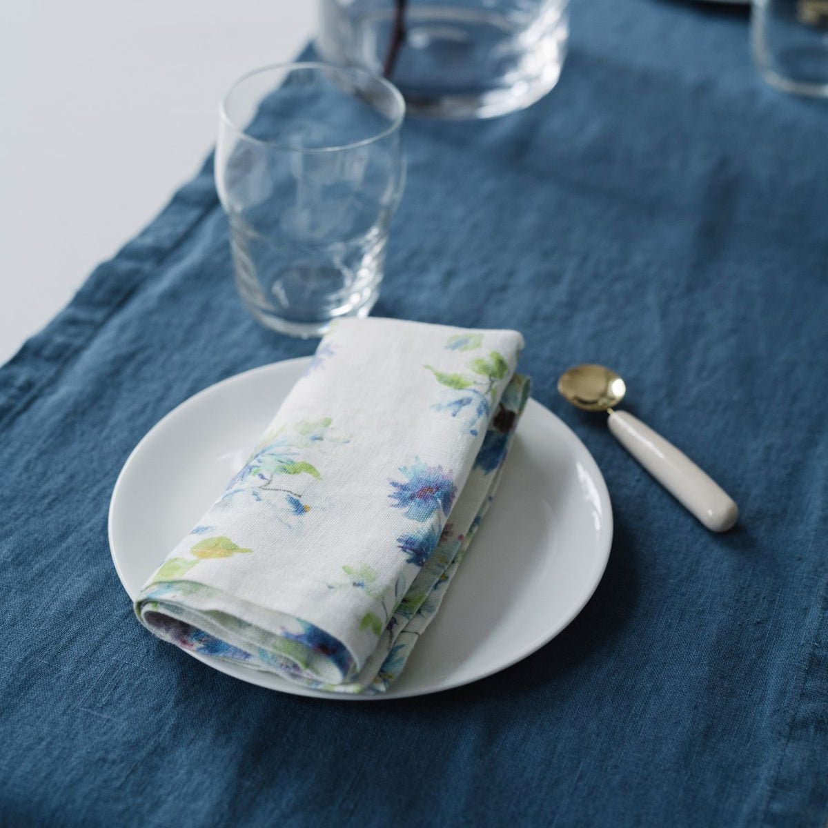 9. Floral linen napkin on a white plate with a decorative spoon on a dark blue placemat