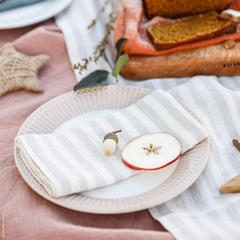 1. Striped linen napkin folded on a white plate with apple slice and decorative acorn on a festive table setting