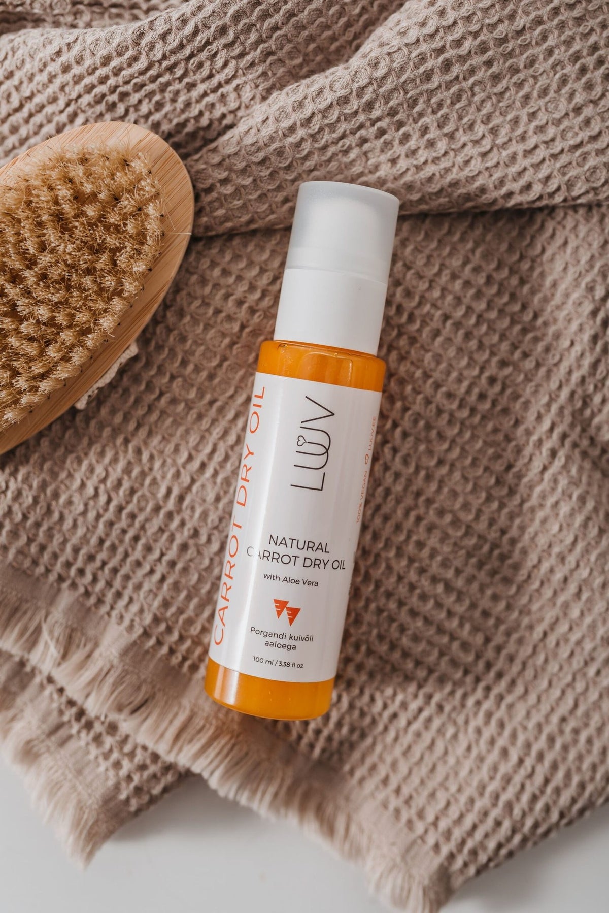 6. LUUV Carrot Dry Oil bottle on a textured fabric with a wooden brush, highlighting natural skincare