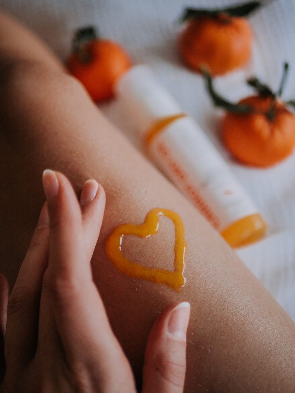 7. Close-up of LUUV Carrot Dry Oil applied in heart shape on skin, with blurred background of oranges