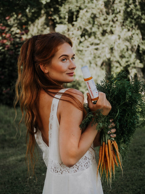 2. Woman holding LUUV Carrot Dry Oil and fresh carrots in a garden setting, wearing a white dress
