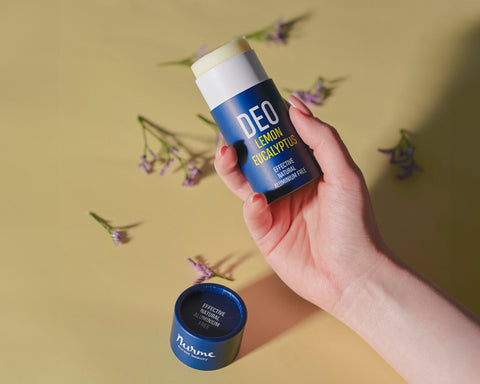 1. Hand holding Nurme natural deodorant with lemon and eucalyptus on a yellow background with flowers