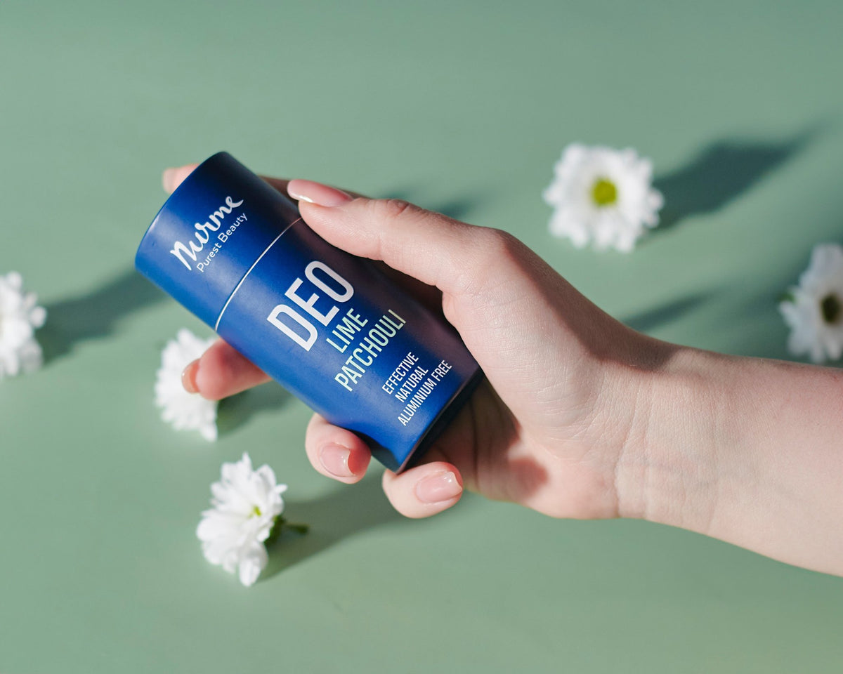 7. Hand holding Nurme Lime & Patchouli deodorant with white flowers on a green background