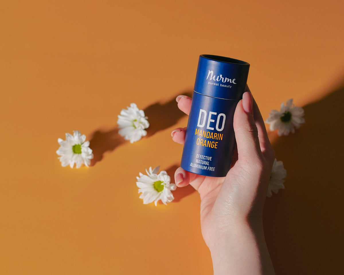 5. Hand holding Nurme mandarin and orange deodorant on orange background with white flowers