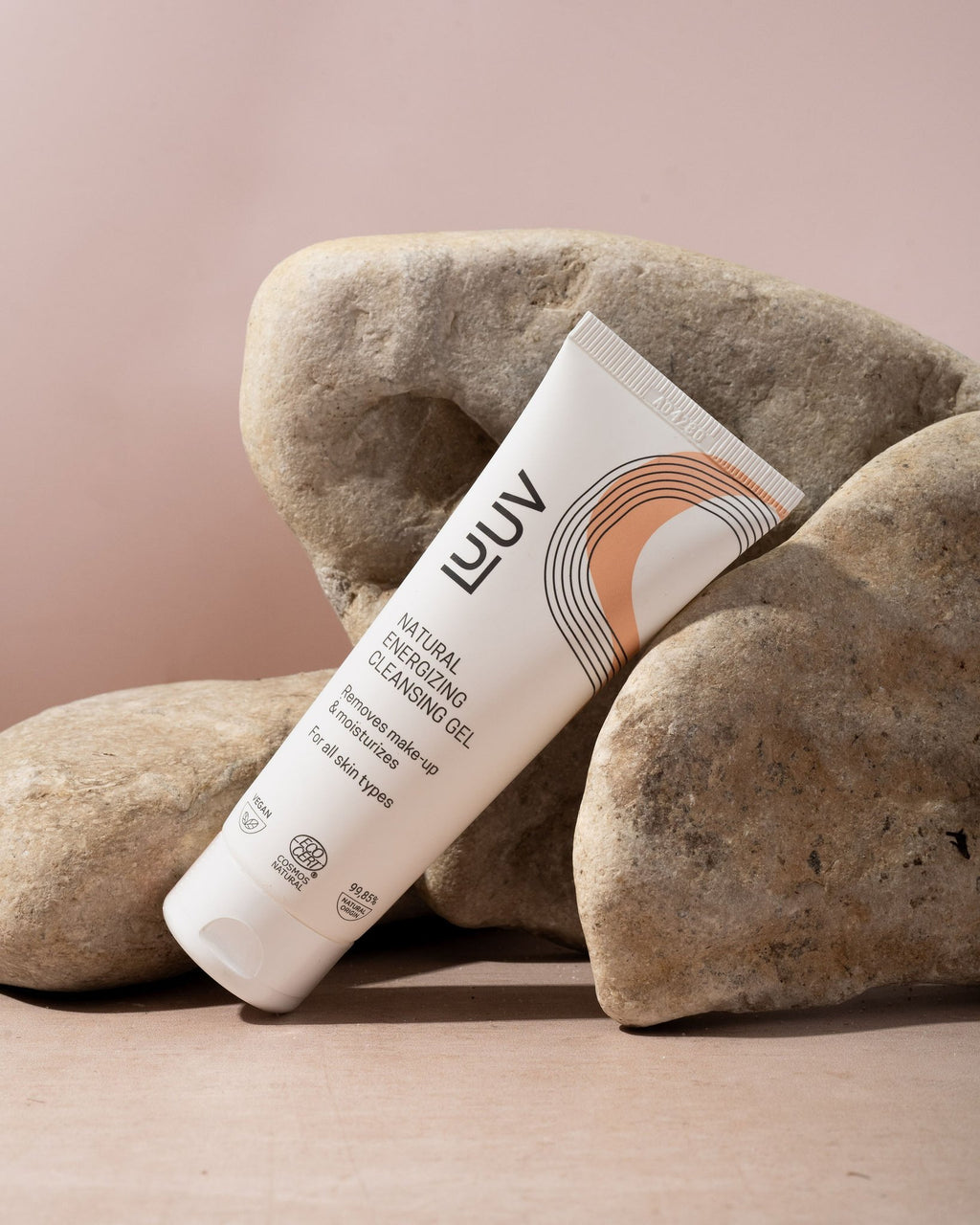 1. LUUV Natural Energizing Cleansing Gel tube with orange design leaning on rocks against a soft pink background