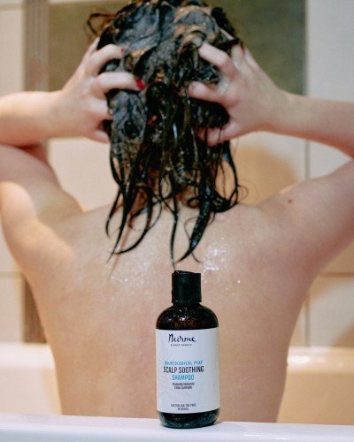 6. Woman washing hair with Nurme scalp soothing shampoo in a bathroom, with the shampoo bottle in the foreground