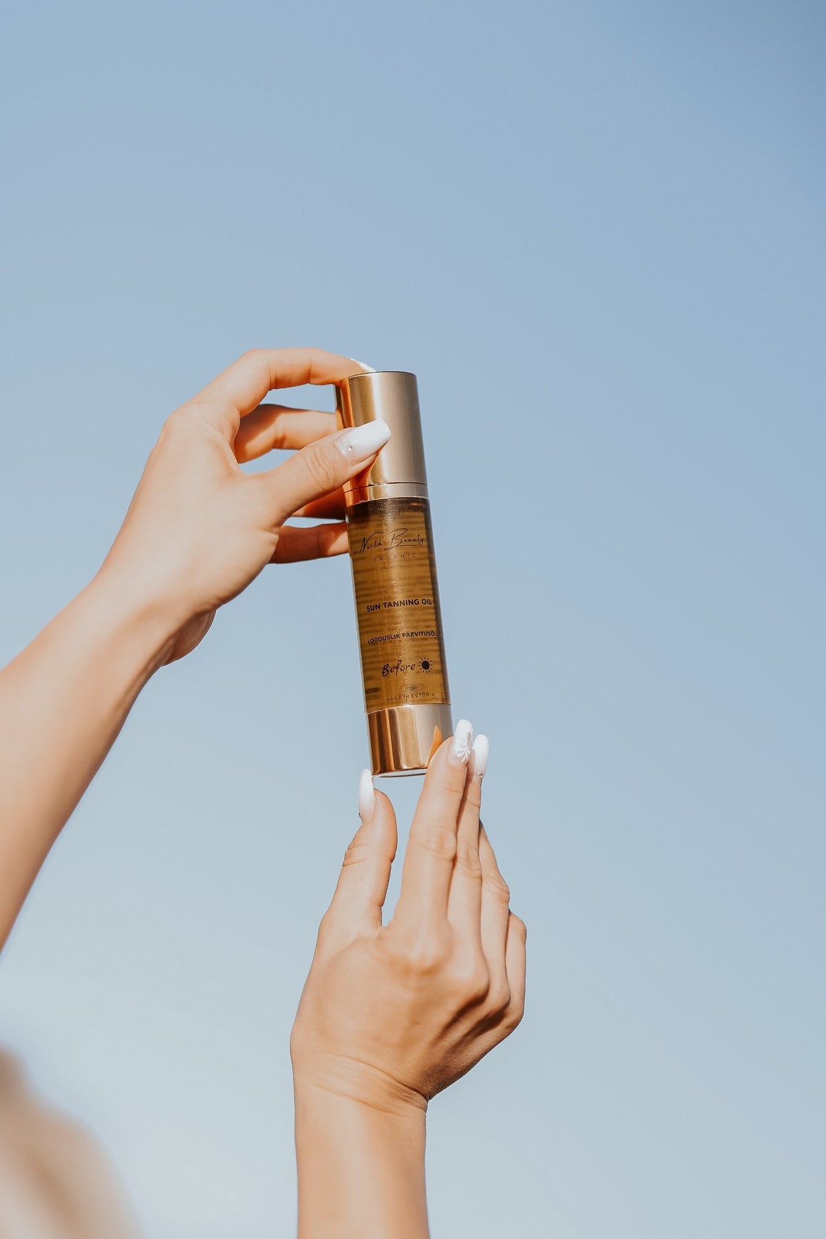 2. Close-up of North Beauty Natural Tanning Oil bottle held against a clear blue sky, highlighting packaging and design