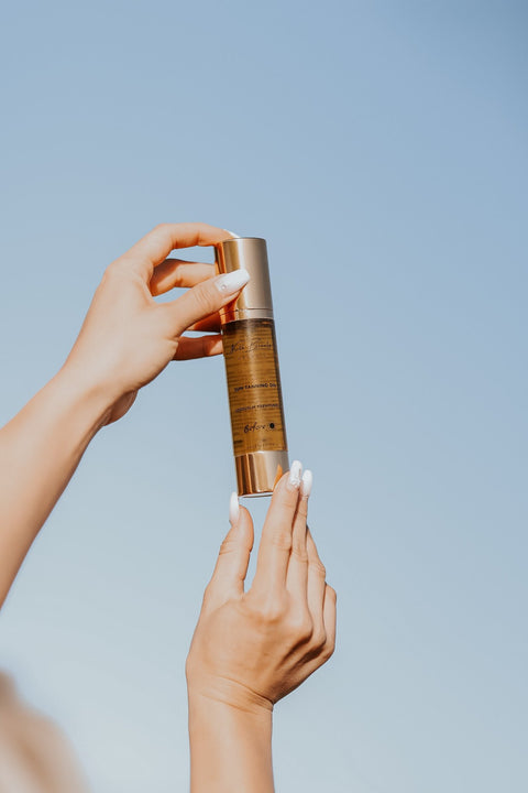 2. Close-up of North Beauty Natural Tanning Oil bottle held against a clear blue sky, highlighting packaging and design