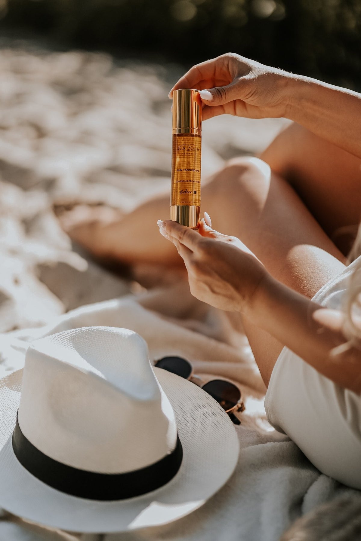 1. Woman holding North Beauty Natural Tanning Oil on a sandy beach, showcasing sun-kissed skin and summer essentials