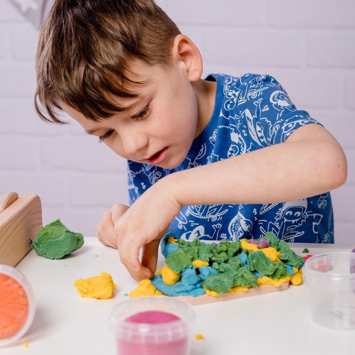 5. Boy focused on shaping Neogrün Easy Clay in green and yellow on a white table