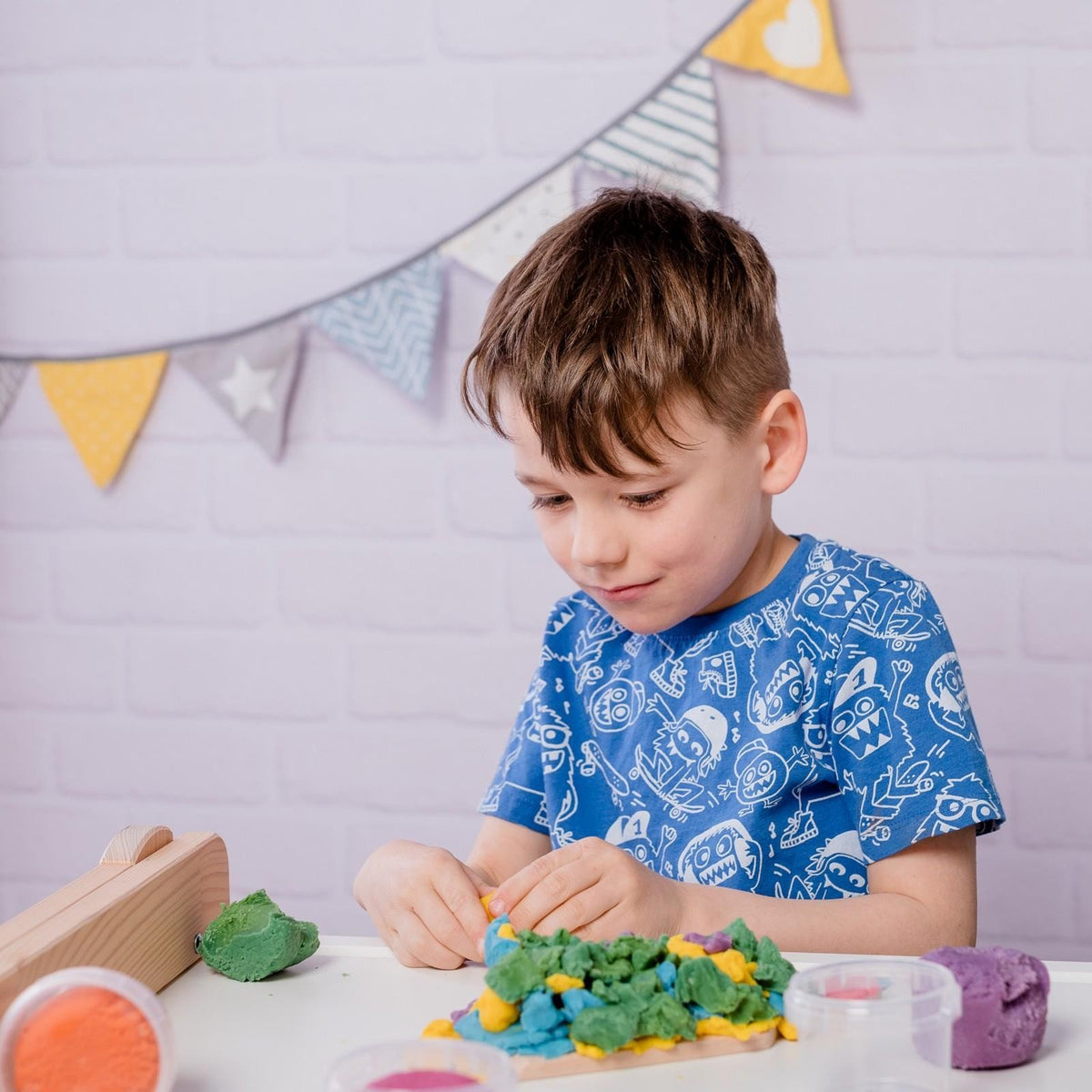 4. Young boy in blue shirt playing with Neogrün Easy Clay in a colorful setting with bunting in background