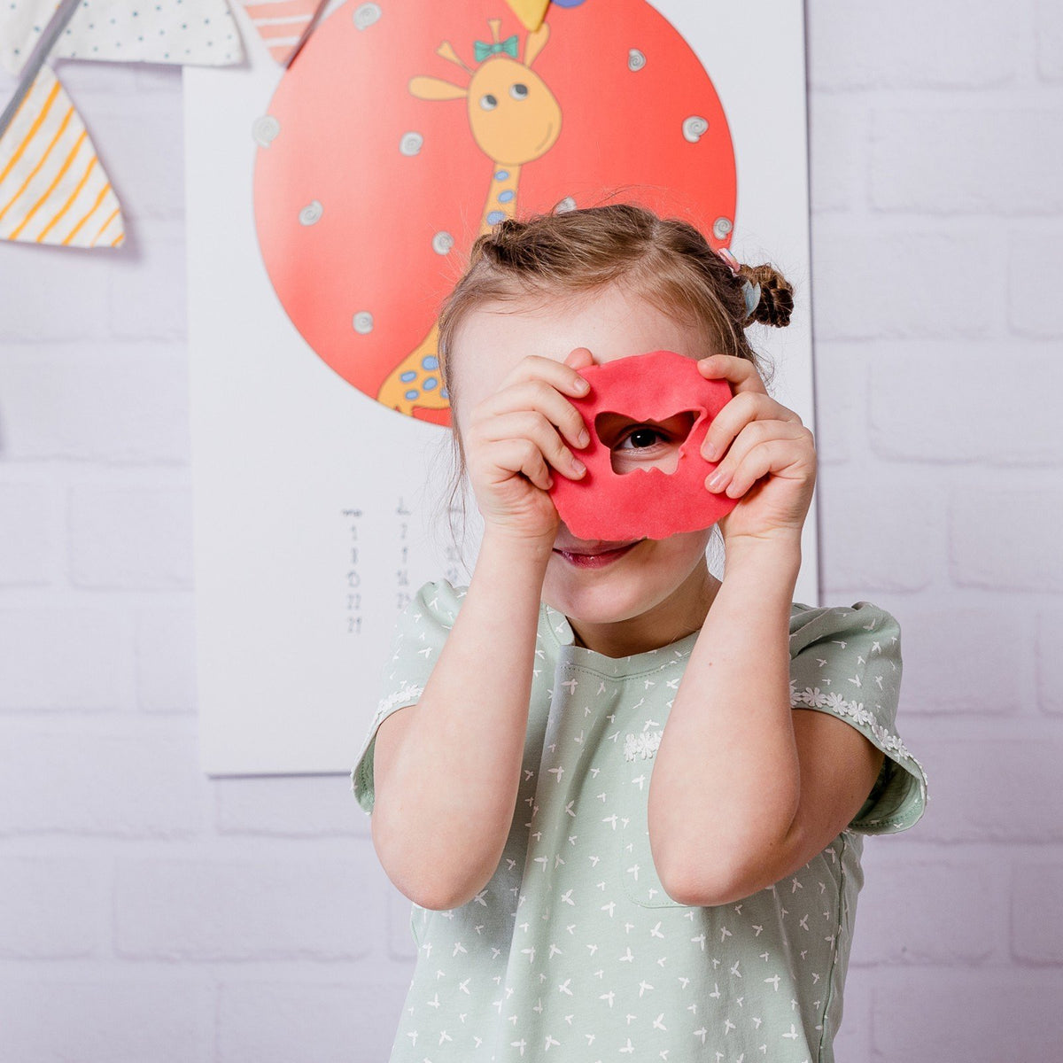 1. Child holding red Neogrün Easy Clay in front of face, wearing a light green shirt with a giraffe poster in the background