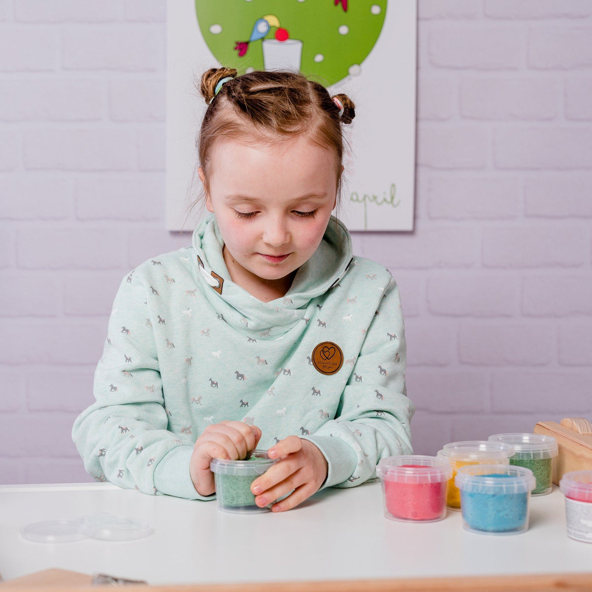 1. Young girl playing with Neogrün Easy Clay in green, wearing a light green hoodie with a playful background