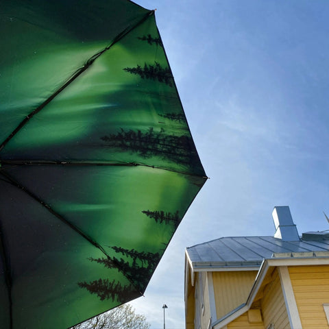 2. Norrsken umbrella with Northern Lights design open against blue sky and yellow house