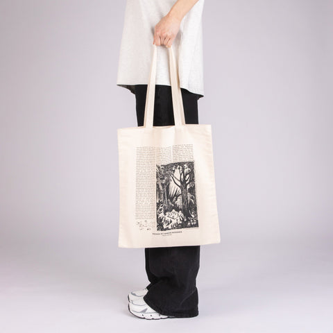 1. Unisex white Moomin Novels tote bag held by a model, featuring black print design, in studio setting