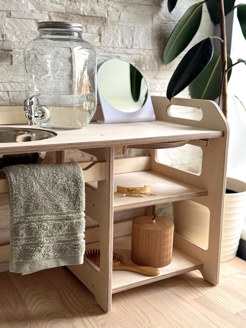 1. Montessori wooden washbasin with storage, featuring a towel, mirror, and plant in a cozy indoor setting