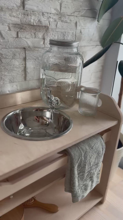 3. Detail of steel bowl and glass jar on Montessori washbasin, highlighting the wooden structure and towel