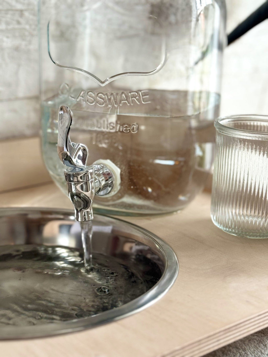 9. Close-up of water flowing from glass jar into steel bowl on Montessori washbasin