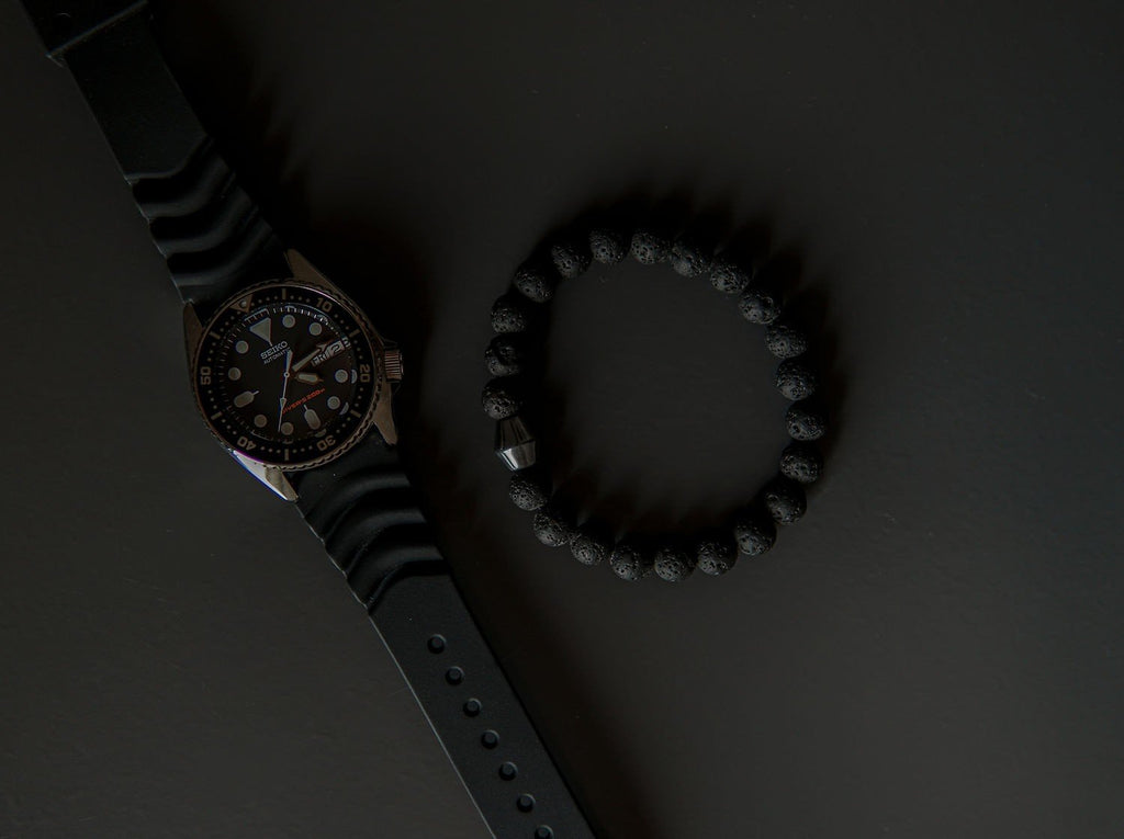 4. Flat lay of Obsidian Lava Stone Bracelet by Canary Lava next to a watch, emphasizing polished lava rocks and Obsidian stone