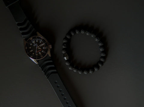 4. Flat lay of Obsidian Lava Stone Bracelet by Canary Lava next to a watch, emphasizing polished lava rocks and Obsidian stone