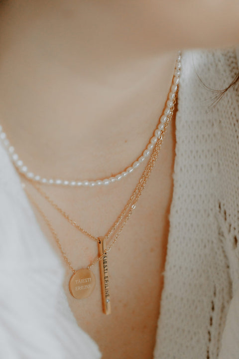 1. Women's layered necklace set featuring Olla's freshwater pearl necklace in gold, styled with additional gold chains, worn with a white knit top