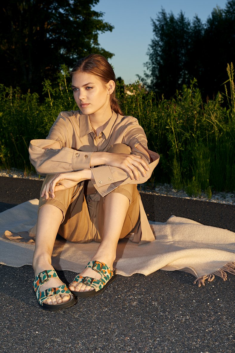 1. Woman wearing Omaking Meeliku Sandals in multicolor, sitting outdoors on a blanket